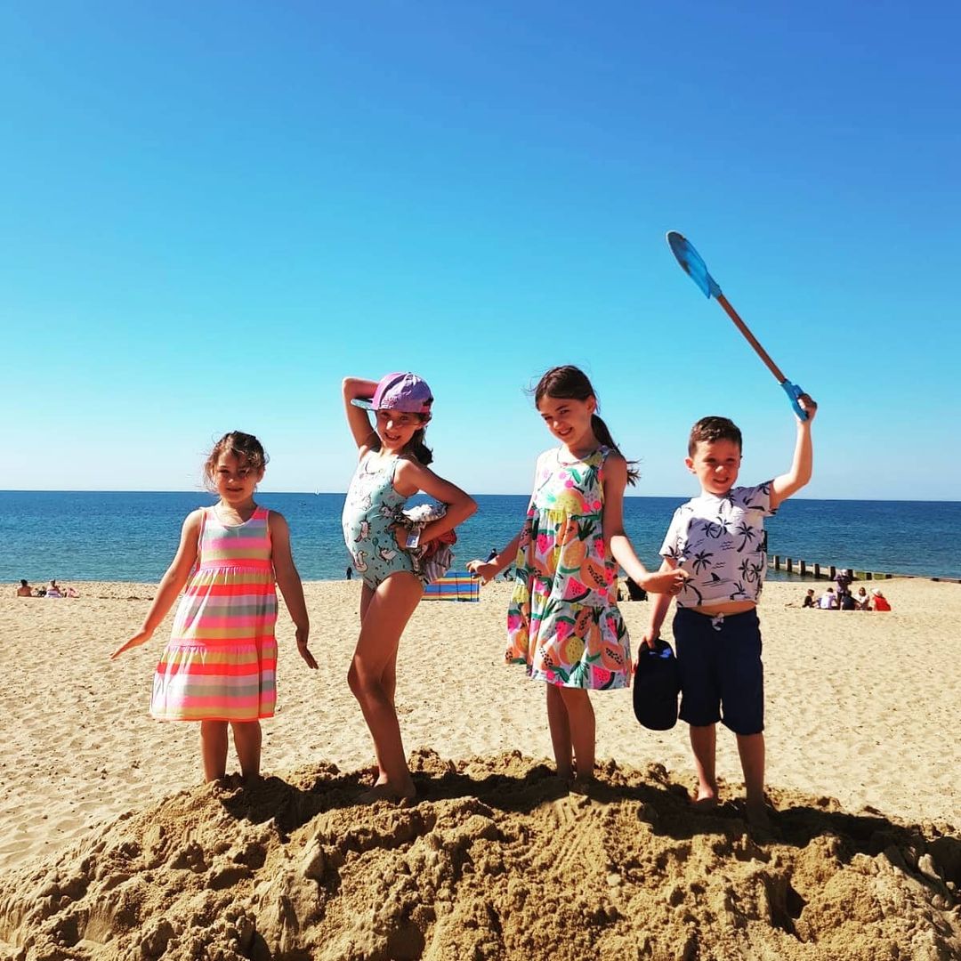 Three female children and a male child strike a pose on top of sand heap at Southbourne Beach in Bournemouth