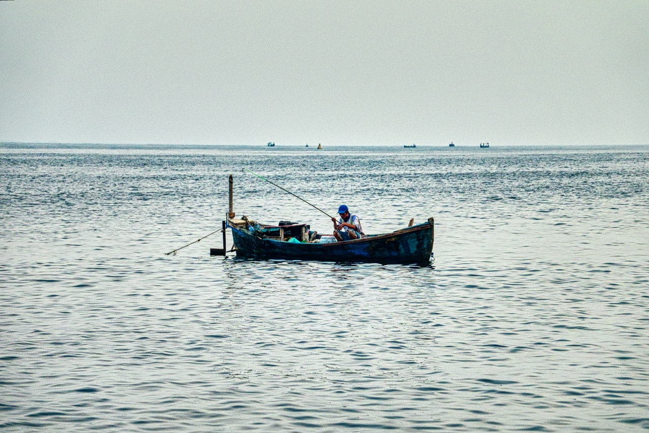 Man Sitting on Fishing Boat on Calm Body of Water