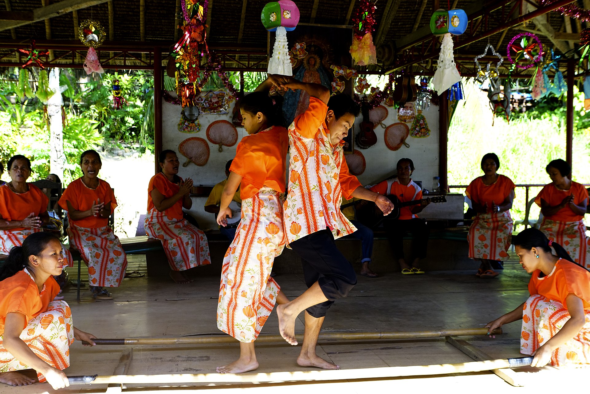 A man and a woman doing the Tinikling Dance of the Philippines using bamboo sticks