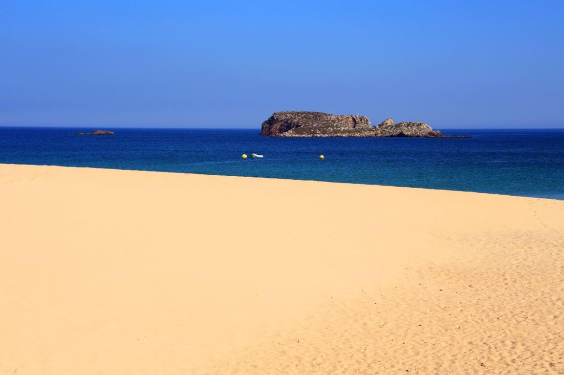 Praia Do Martinhal boasts light brown sand, emerald blue ocean, and an island in the middle