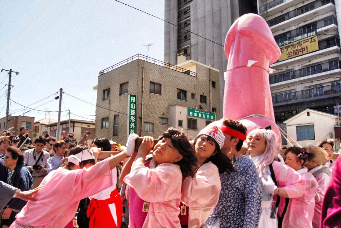 A group of people in the festival parade holding a pink penis statue