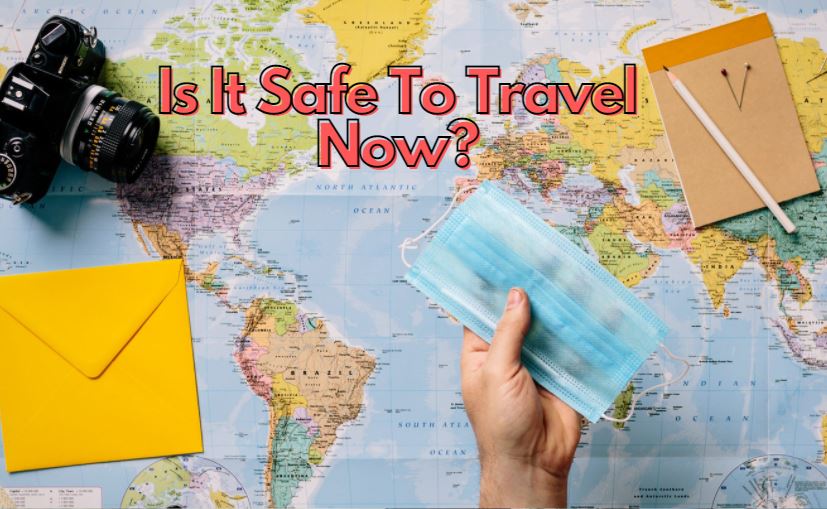 a map with a camera, envelope, notebook, pen and a hand holding a face mask with words is it safe to travel now?