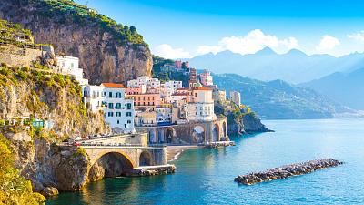 A beautiful scene of Italy with a boat on the lake and a white fort type building and some colorful houses in the background 