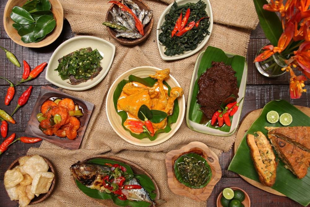 Indonesian Padang includes fish, red chilies, chicken, bread, and a lot more on banana leaves on a dark brown wooden table