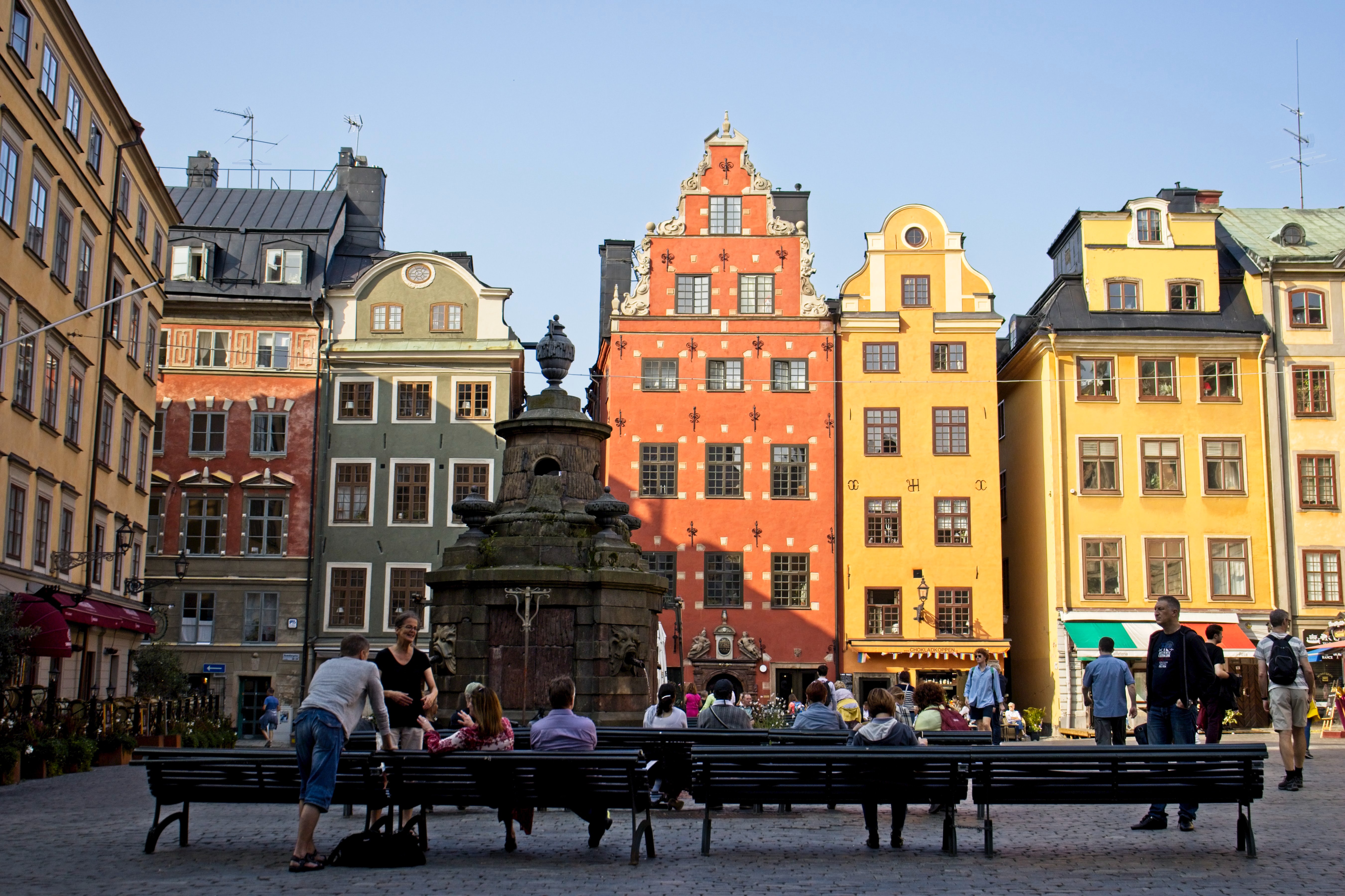 A shot of  Gamla Stan, Stockholm with different colored buildings and people sitting on park benches