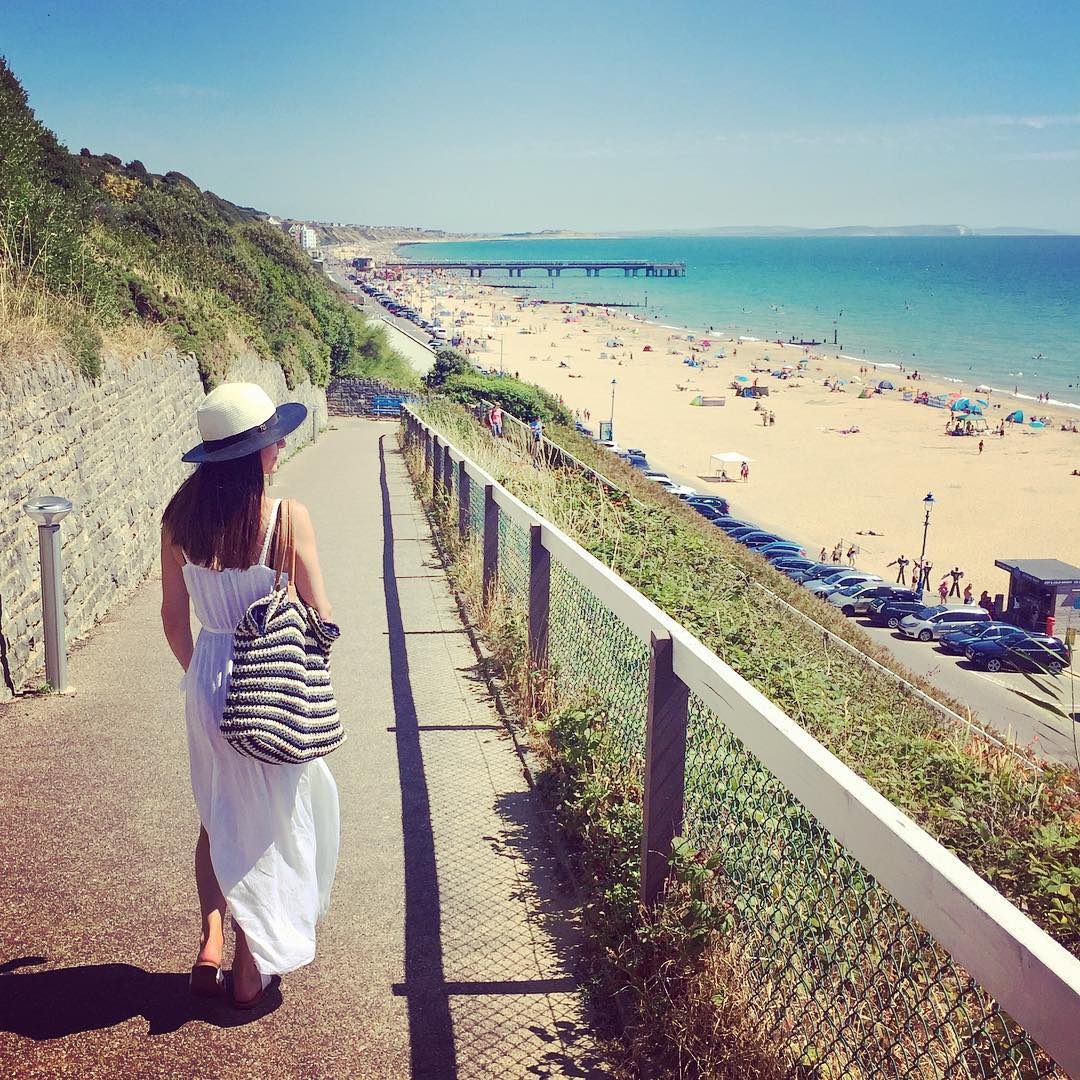 A woman in white dress and hat walking her way to Bournemouth Beach