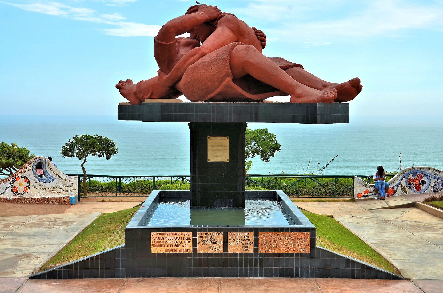 A park with a red romantic statue of a man and woman kissing each other