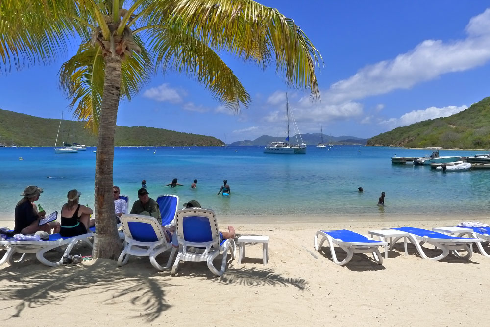 Pirate’s Bight beach, sea view, Norman Island with people sitting on beach chairs and some are swimming