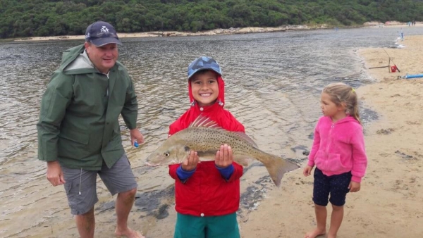 A family enjoying their stay at the natures valley and a male child is smiling at the camera while holding a large fish