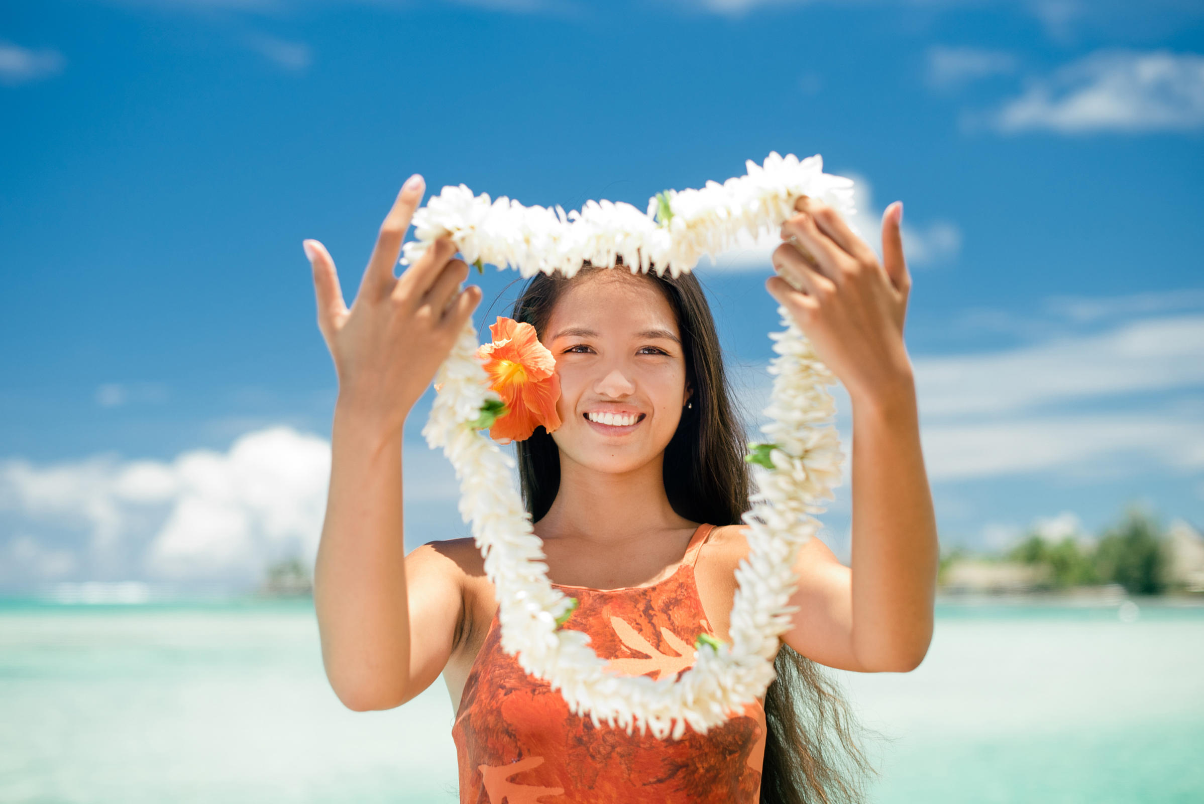 A Tahitian woman welcoming tourists while holding a big flower necklace