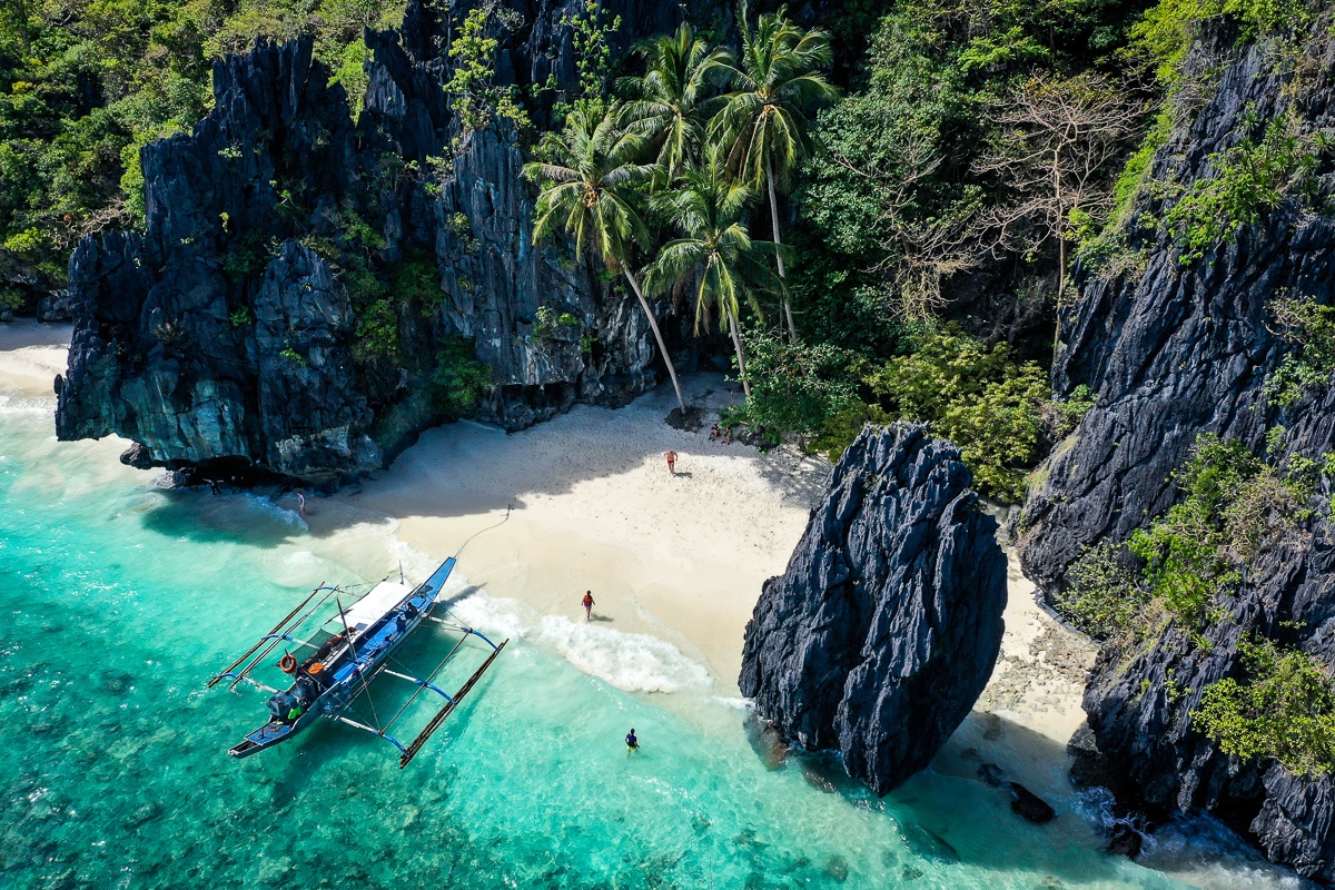 El Nido Palawan beach with big stone formations, boat and people walking along the sand