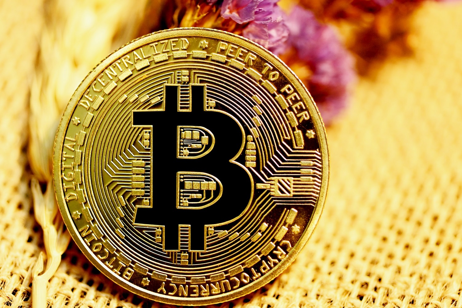 A gold Bitcoin, with the words ‘cryptocurrency, digital, decentralized, peer to peer’ engraved around