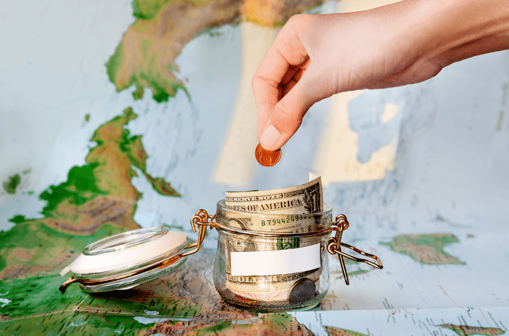 A man putting a coin in a glass bottle with money with a map underneath