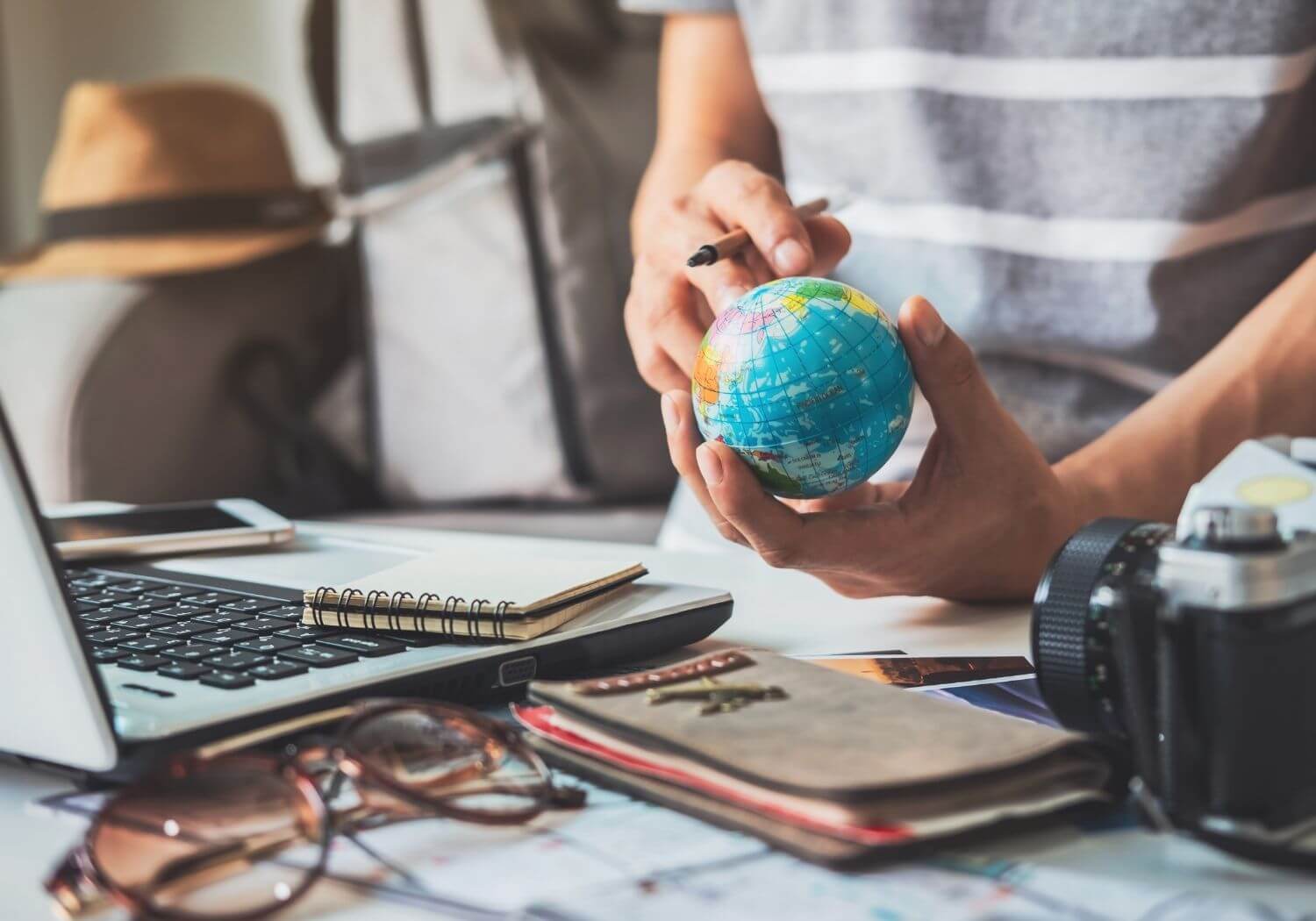 At the office, a man is holding a small globe and on his right hand is a pen with a laptop and other things on the table