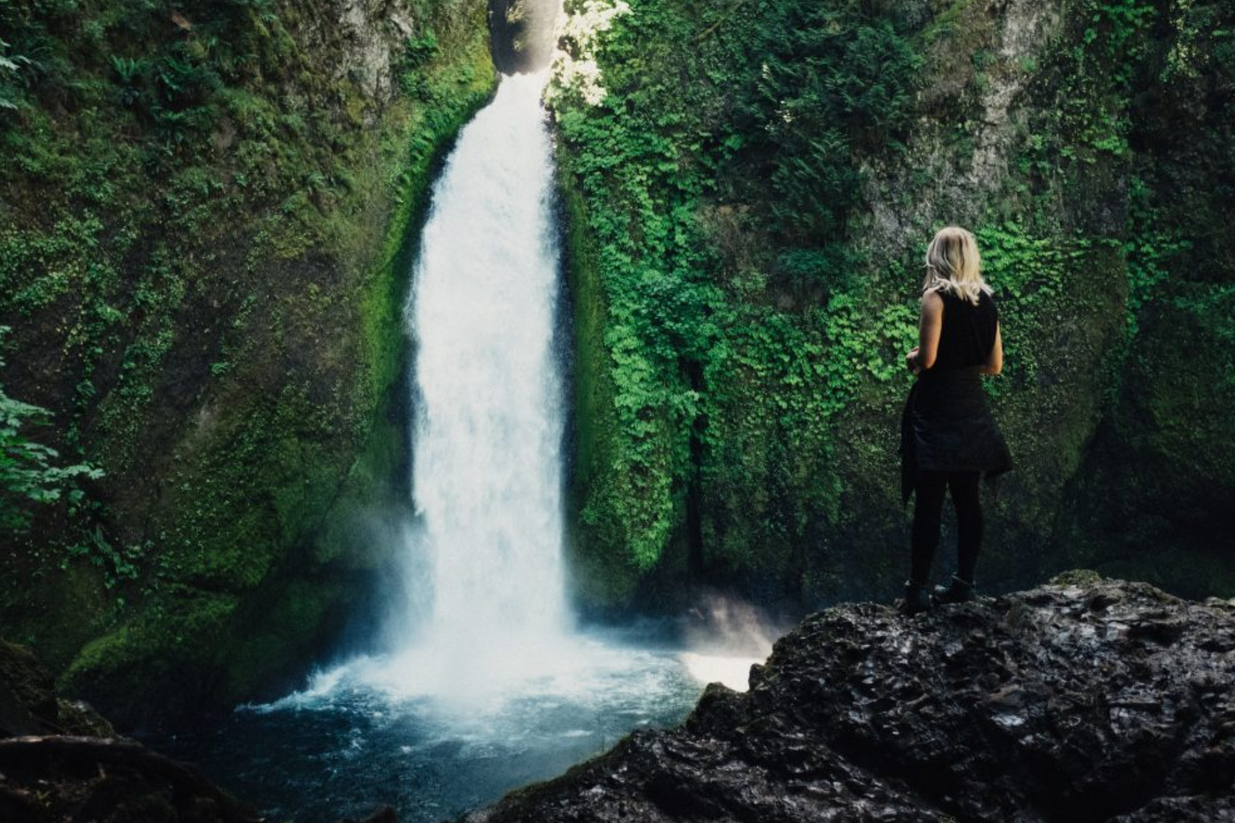 A woman stands on a rock in front of the falls