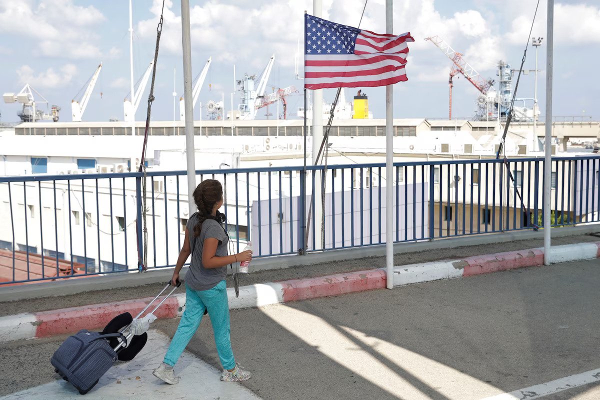 A woman walking on a walkway with her luggage as the U.S. flag flies by the side
