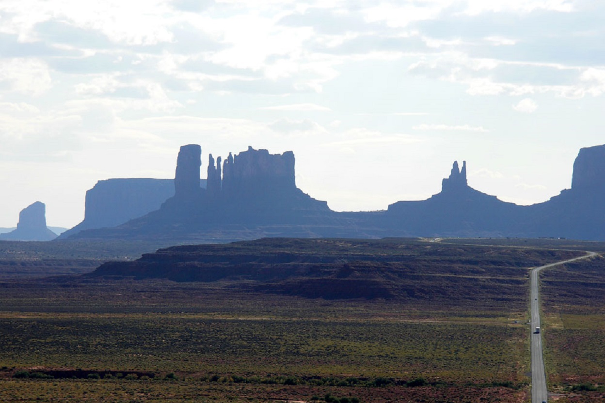 A misty view of Monument Valley in Arizona, with a lone vehicle traversing the narrow U.S.-163 Road