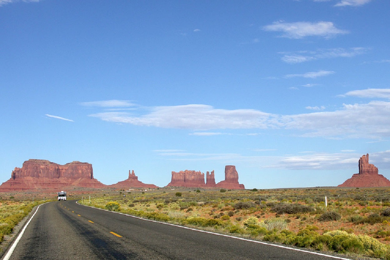 A panoramic view of Monument Valley in daytime in Arizona from U.S.-163 Road, with one vehicle traveling